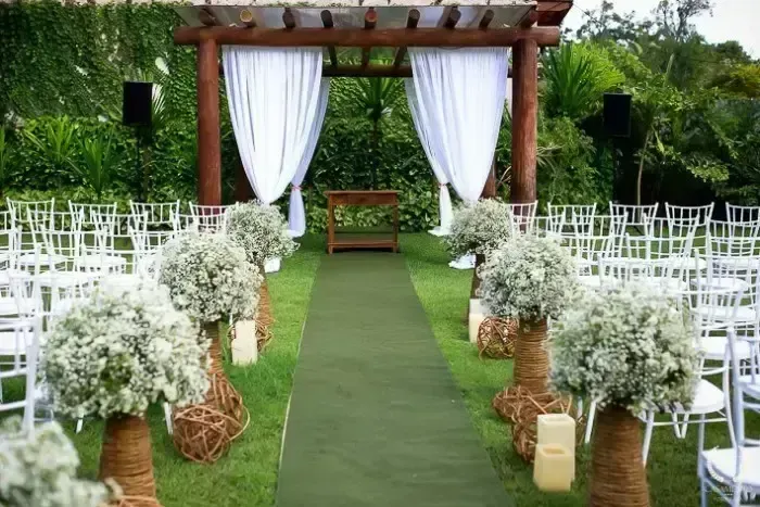 Cerimônia ao ar livre decorada com flores brancas e cadeiras brancas para um casamento na natureza, com uma passarela central e um ambiente ao ar livre tranquilo.