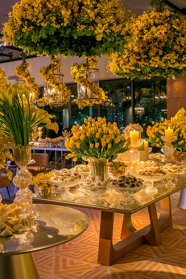 Decoração de festa com arranjos de flores amarelas, velas e iluminação suave, ideal para celebrações sofisticadas em ambiente elegante.