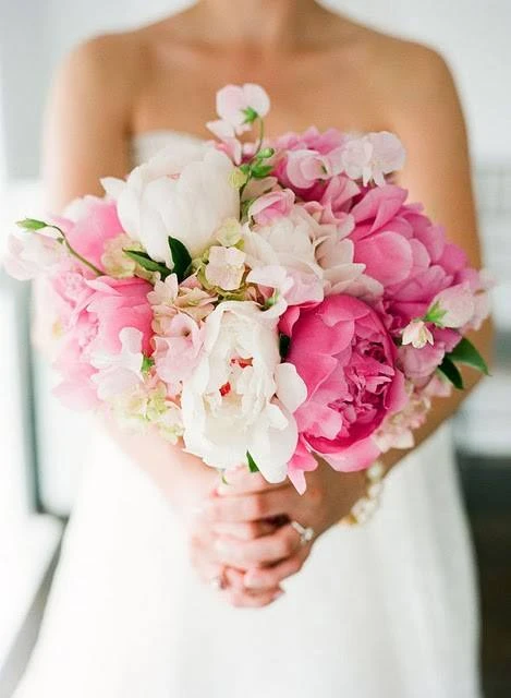 Mulher segurando um buquê de flores rosa e branco, vestindo vestido de noiva, em um cenário de casamento.