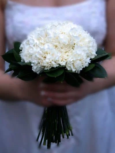 Buquê de flores brancas, ideal para casamento ou celebração especial, com flores delicadas e folhas verdes, sendo uma escolha elegante para ocasiões especiais.