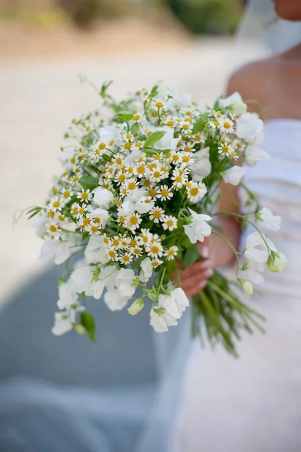 Buquê de flores com margaridas brancas e dentes de leão, ideal para casamentos ou ocasiões especiais ao ar livre.