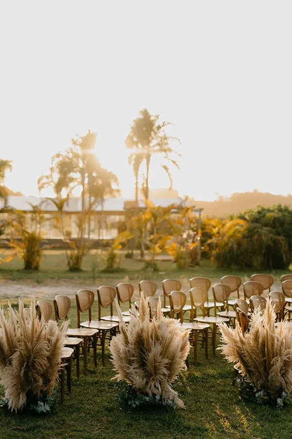 Cerimônia ao ar livre ao pôr do sol, com cadeiras dispostas em círculo e arranjos de flores secas em um cenário natural.