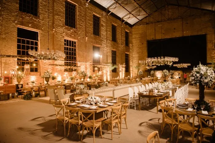 Imagem de uma decoração de evento elegante em um espaço industrial com mesas decoradas com flores, velas e iluminação suave, ideal para casamentos e festas sofisticadas.