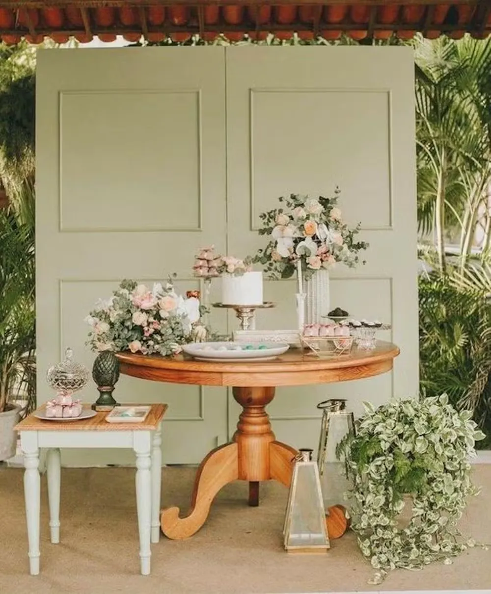 Decoração de casamento com flores, velas e vasos em um cenário ao ar livre, destacando um fundo de painéis verdes e plantas tropicais.
