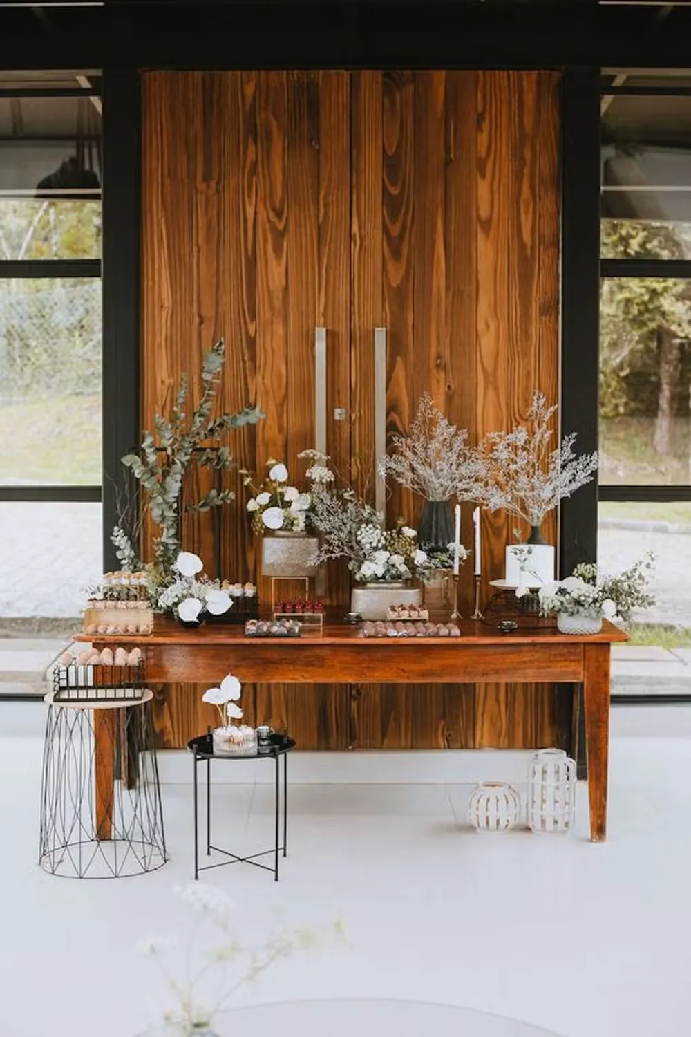 Decoração minimalista com mesa de madeira e arranjos florais brancos e verdes, ideal para eventos especiais ou celebrações ao ar livre.