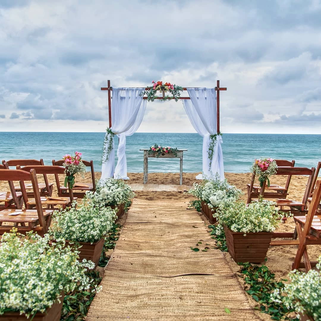 Cerimônia de casamento ao ar livre na praia com altar decorado, cadeiras de madeira e flores, ideal para noivos que desejam uma cerimônia ao ar livre e pé na areia.