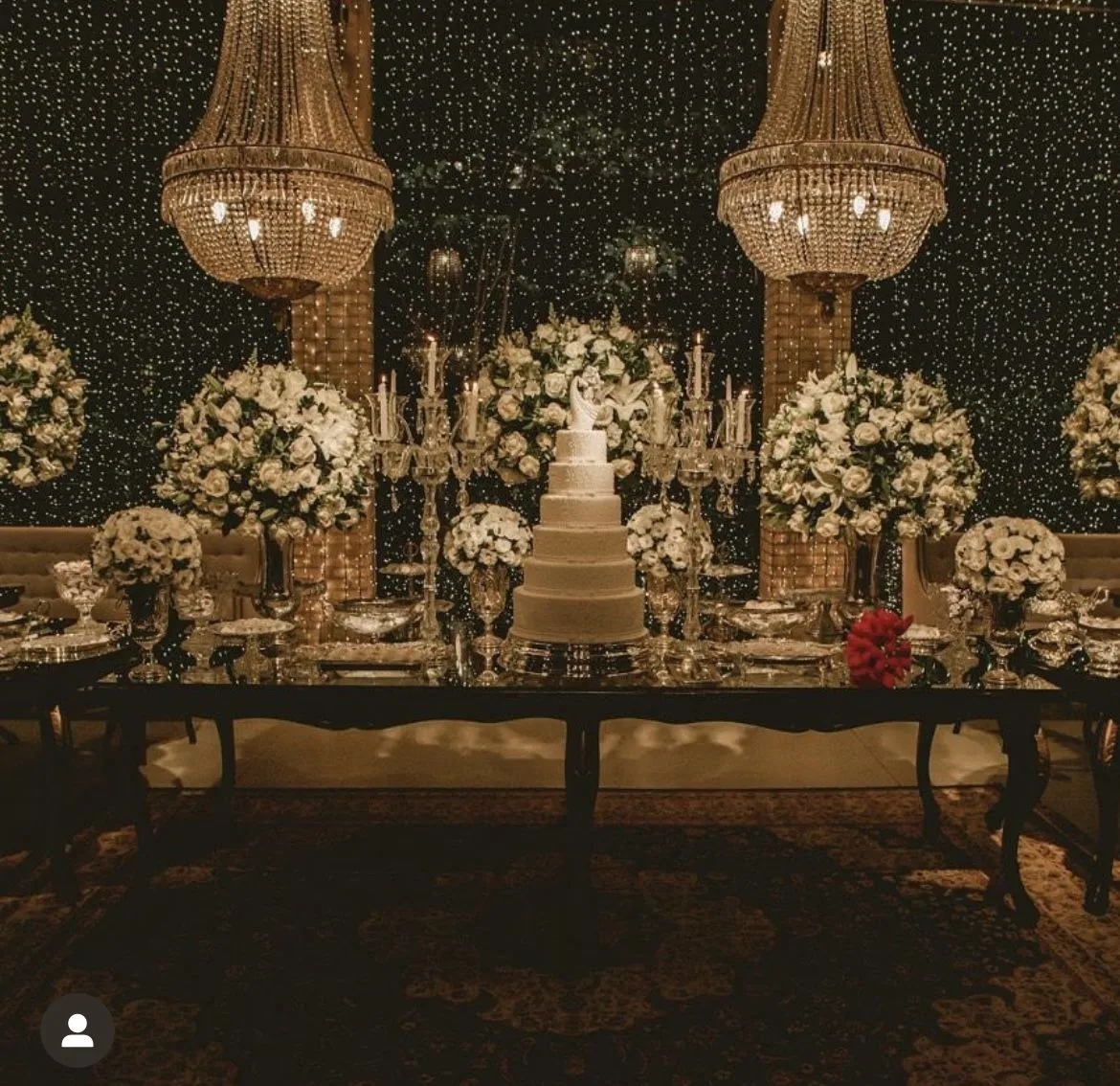 Decoração de festa de casamento com bolo de casamento, arranjos florais brancos, velas,lustres de cristal e uma mesa sofisticada, ideal para comemorações elegantes.