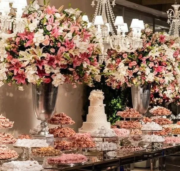 Decoração de casamento elegante com arranjos florais rosa e branco, bolo de casamento e doces decorativos em ambiente sofisticado.