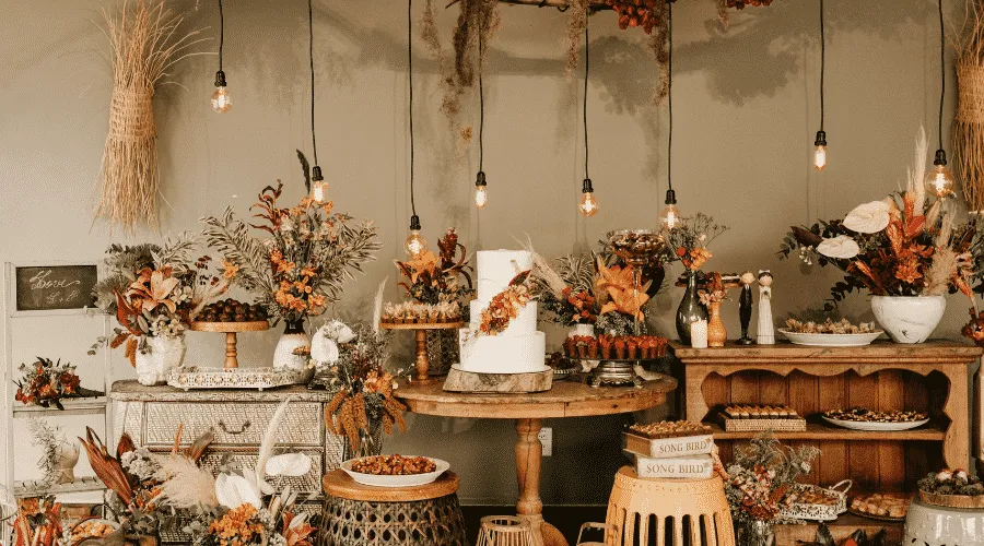 Decoração de festa rústica com arranjos florais em cores quentes, velas e objetos de madeira, ideal para celebrações ao ar livre ou festas temáticas.
