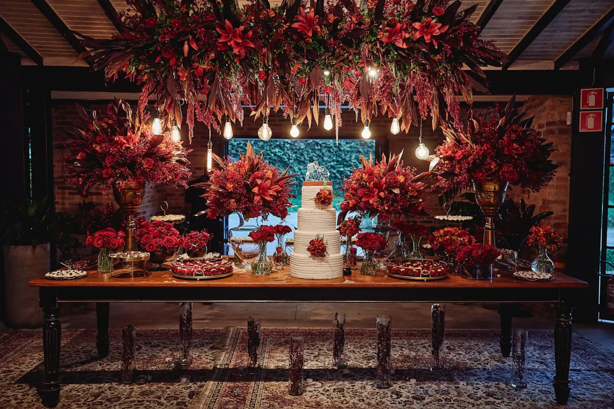 Decoração de festa de casamento com muitas flores vermelhas, bolo de casamento no centro, iluminação suave e ambiente sofisticado.