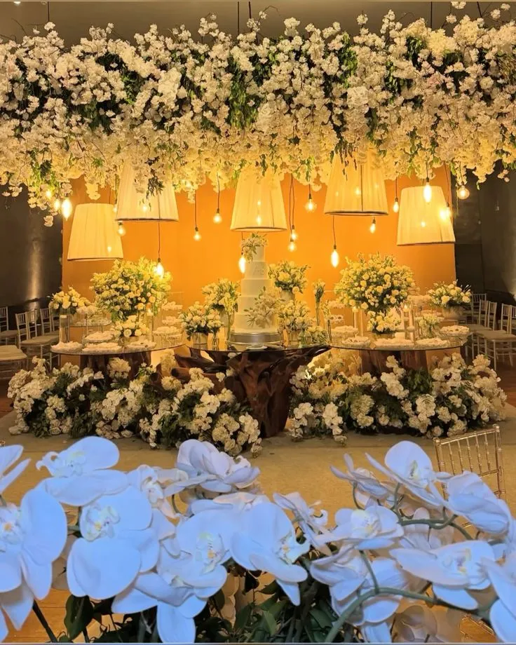Decoração de casamento elegante com flores brancas, lustres suspensos e iluminação suave em um ambiente sofisticado.