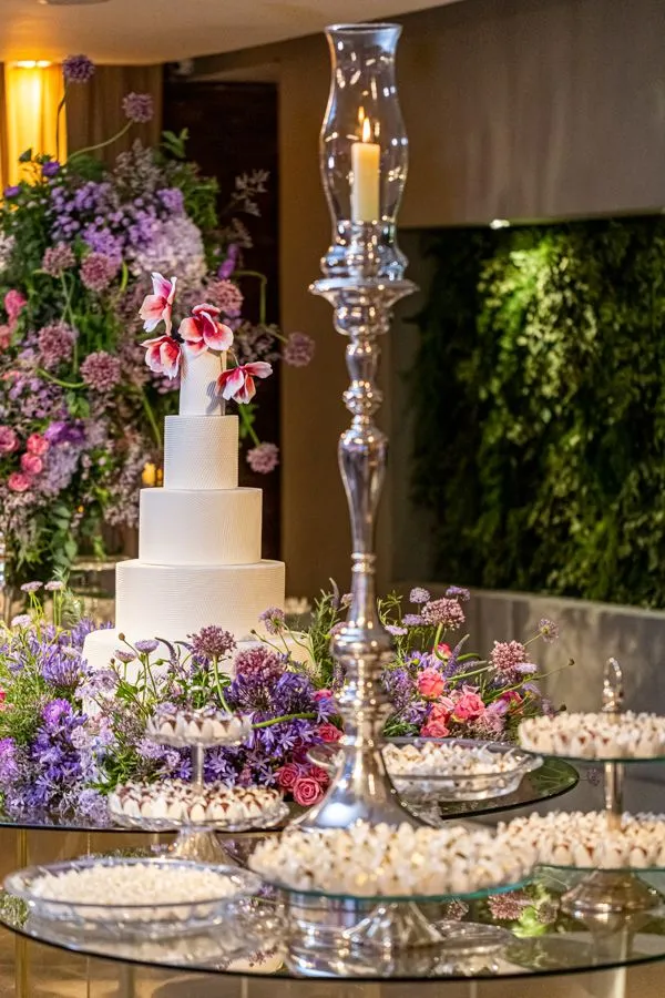 Decoração de casamento com bolo de três camadas, flores naturais coloridas e velas em ambiente elegante e sofisticado.