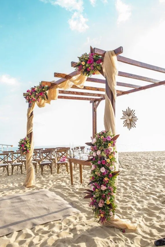 Cerimônia de casamento na praia com decoração de flores, estrutura de madeira e vista para o mar, ideal para casamento ao ar livre.