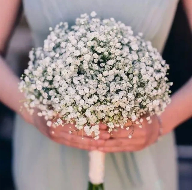 Ramo de flores brancas delicadas sendo segurado por mãos em ambiente ao ar livre, ideal para decoração de casamento ou ocasião especial.