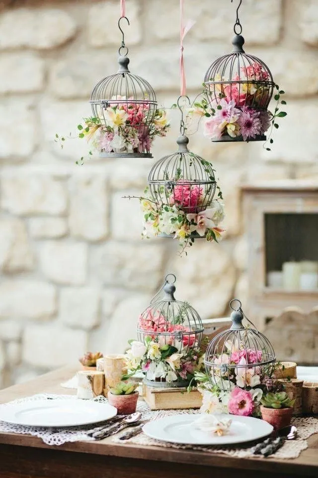 Decoração elegante com gaiolas de ferro decoradas com flores cor de rosa e branca, ideal para eventos românticos ou casamento ao fundo de parede de pedra.