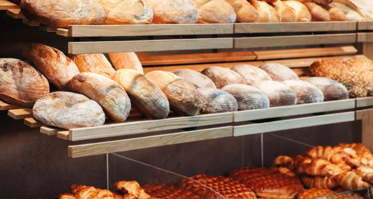 Padarias com variedades de pães artesanais e croissants expostos em prateleiras de madeira, criando uma atmosfera acolhedora e saborosa.