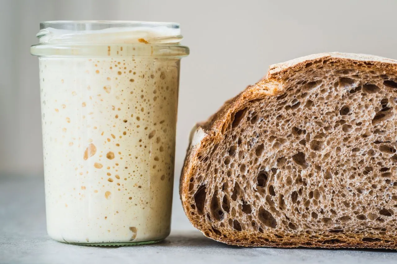 Pote de fermento natural ao lado de um pão integral