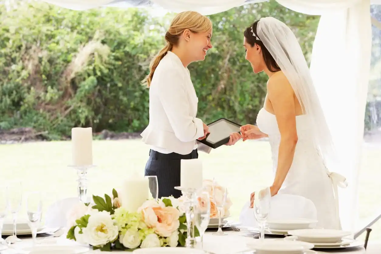 Cerimonialista e noiva no dia do casamento, com uma cerimônia ao ar livre rodeada de natureza, trocando alianças e comemorando o momento especial.