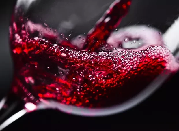 vinho sendo despejada em um copo, criando bolhas e efervescência na bebida escura e refrescante.
