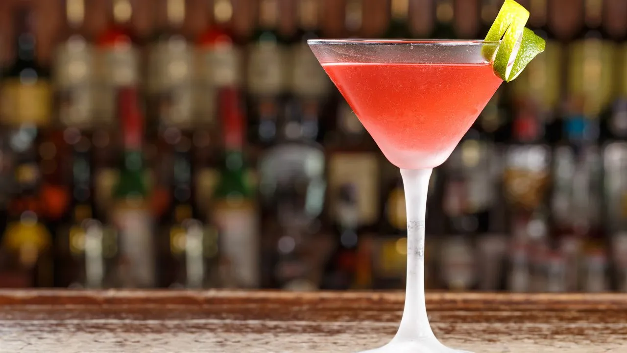Imagem de coquetel rosa servido em taça de martini, decorado com limão na borda, perfeito para drinks de bar ou festas.