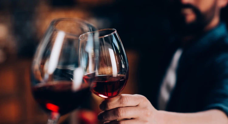 Homem segurando taças de vinho tinto em ambiente aconchegante, perfeito para momentos de relaxamento e confraternização.