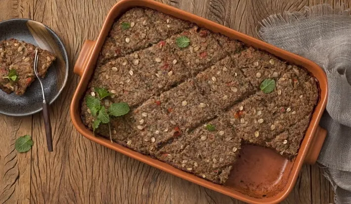 Delicioso prato de kibe de forno com trigo bem temperada e cortada em fatias, servido em uma travessa de cerâmica com ervas frescas para decorativo.