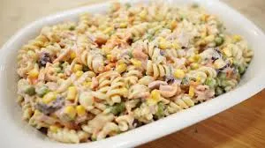 Salada de macarrão com atum e vegetais coloridos e molho em uma travessa branca, ideal para refeições leves e saborosas.