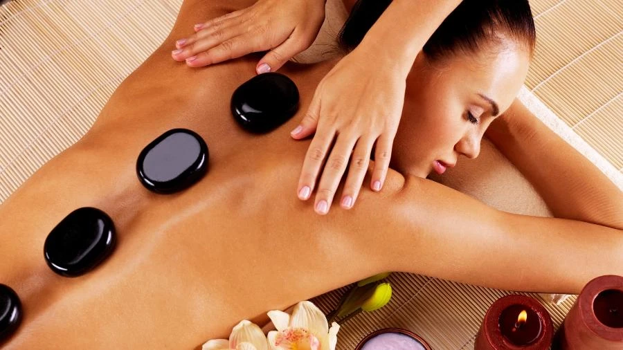Mulher recebendo massagem com pedras quentes nas costas, promovendo relaxamento e bem-estar, em ambiente de spa ou centro de terapias alternativas.