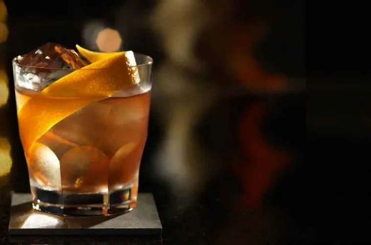 Imagem de um drinque com gelo e uma fatia de limão em um copo de vidro, ambientada sob iluminação suave, ideal para apreciadores de coquetéis sofisticados.