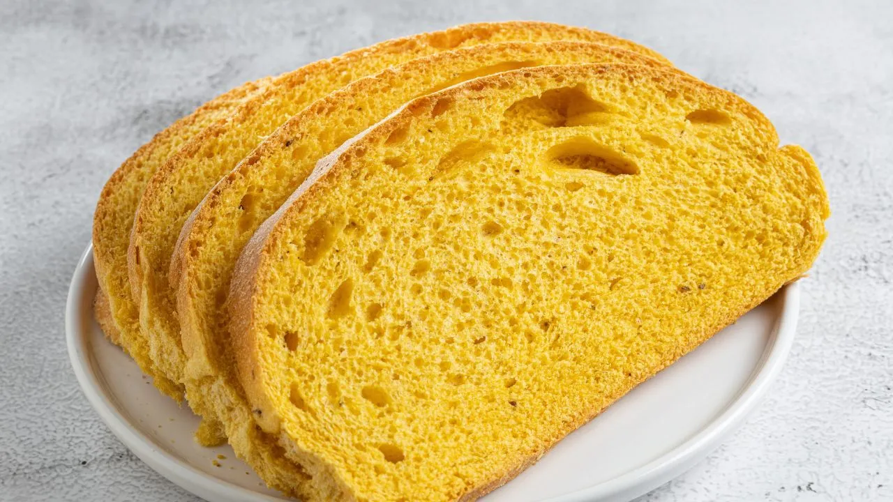 Três fatias de pão de milho dourado em um prato branco, evidenciando a textura macia e a aparência crocante do pão de milho caseiro.