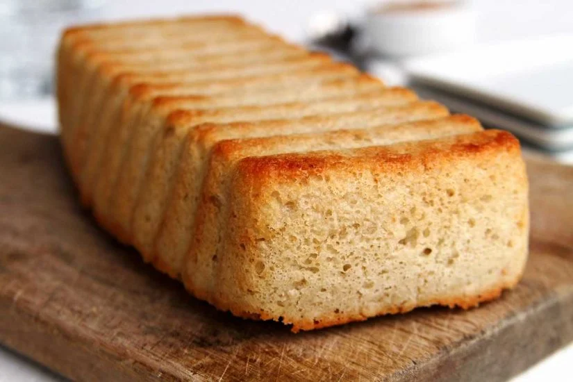 Pedaço de pão de forma dourado e macio, apresentado sobre uma tábua de madeira, ideal para lanches ou cafés da manhã.