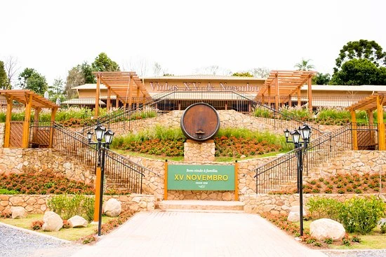Imagem de um parque ou jardim com estrutura de madeira, iluminação de postes, plantas, e uma placa indicando a celebração de XV novembro, ideal para eventos e lazer ao ar livre.