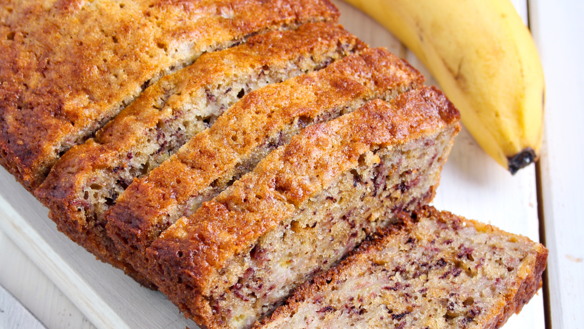 Pão de banana caseiro com textura macia e ingredientes prontos para consumo, acompanhado de bananas maduras ao fundo, ideal para dietary saudável.