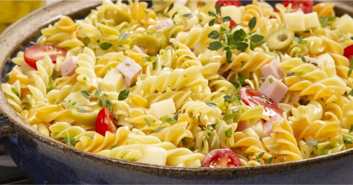 Salada de macarrão rotini com molho, tomates ciliegia, queijo, peito de peru e ervas frescas em uma tigela grande, ideal para refeições leves e saborosas.