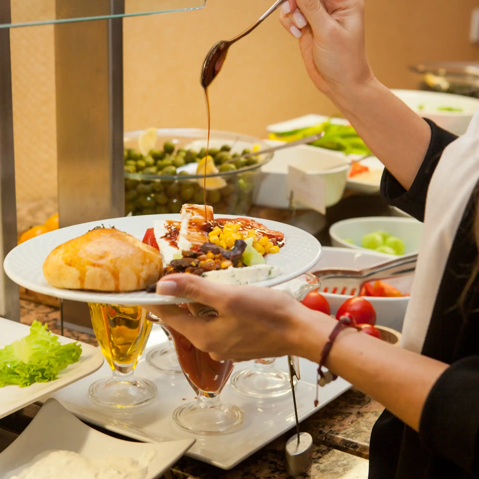 Pessoa servindo uma sobremesa com sorvete, frutas e calda de chocolate em buffet de sobremesas.