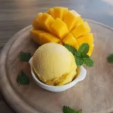 Imagem de sobremesa com sorvete de manga e pedaços de manga fresca, decorada com hortelã fresca, ideal para doces tropicais e sobremesas de verão.