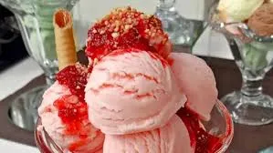 Imagem de uma taça com várias bolas de sorvete, destaque para sorvete de morango com calda e pedaços de biscoito, perfeito para sobremesa refrescante.