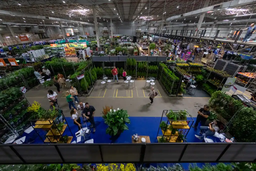 Imagem do interior de um grande centro de jardinagem ou loja de horticultura, com várias plantas, visitantes e corredores.