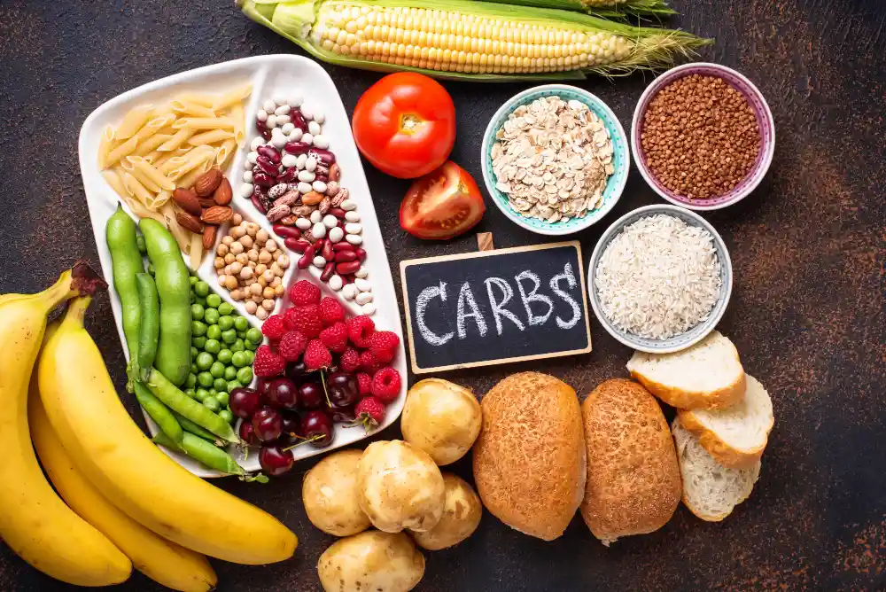 Alimentos ricos em carboidratos, incluindo bananas, pães, arroz, batatas, cereais, legumes e frutas vermelhas, em uma apresentação organizada sobre uma mesa.