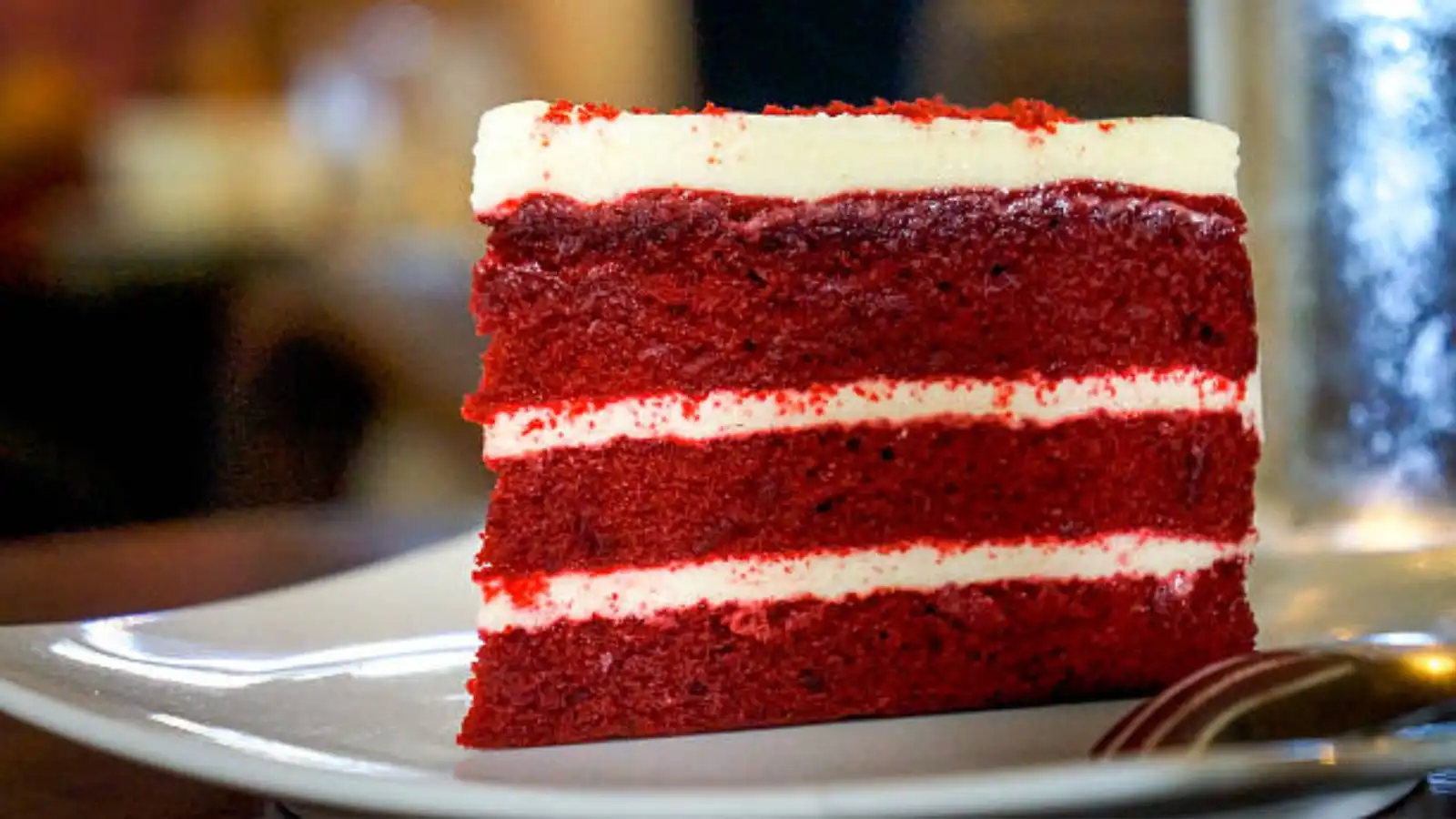 Imagem de uma fatia de bolo de red velvet com camadas de cream cheese, decorado com raspas vermelhas, perfeito para sobremesa.