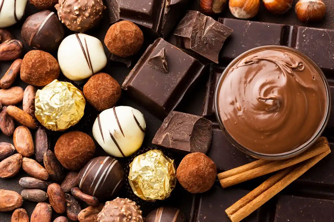 Seleção de chocolates artesanais com diferentes tipos de coberturas, trufas e um pote de creme de chocolate, ideal para quem aprecia doces gourmet.
