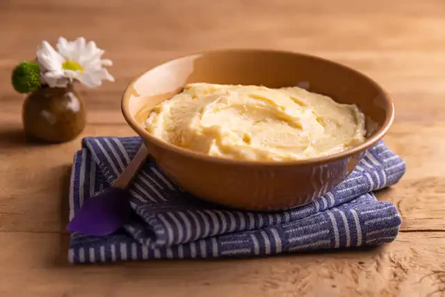 Creme de confeiteiro em tigela de cerâmica sobre um guardanapo azul, ao lado de uma pequena flor branca, em uma mesa de madeira.