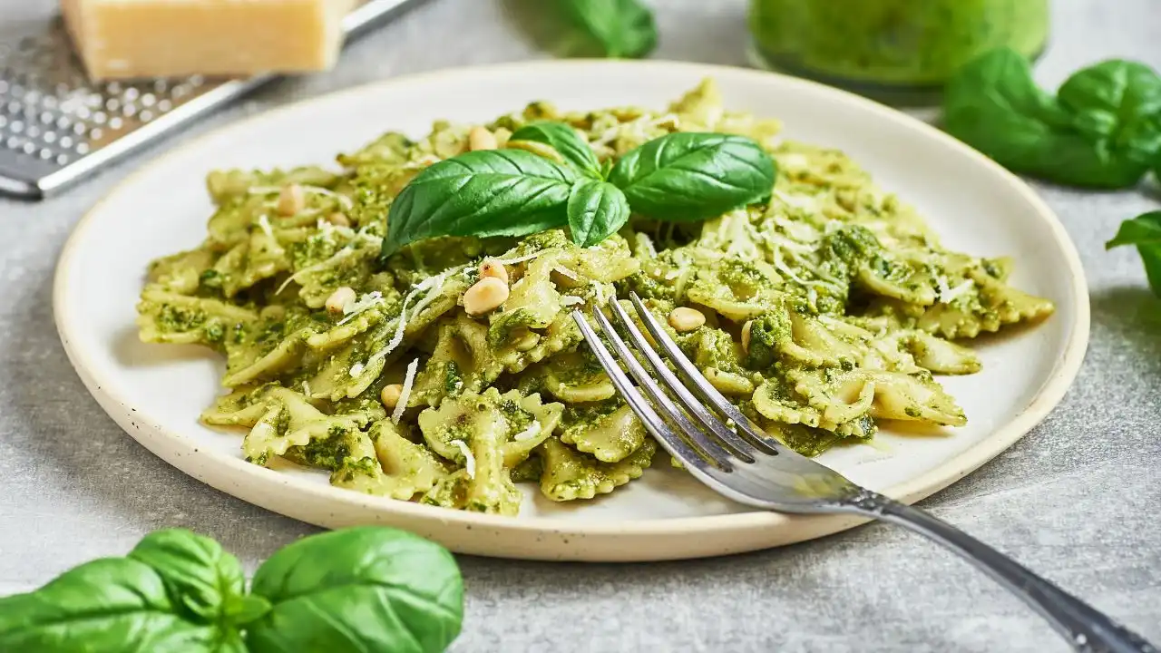 Imagem de uma porção de macarrão com molho de manjericão e queijo, decorada com folhas de manjericão fresco, ideal para quem busca uma receita de macarrão ao pesto.