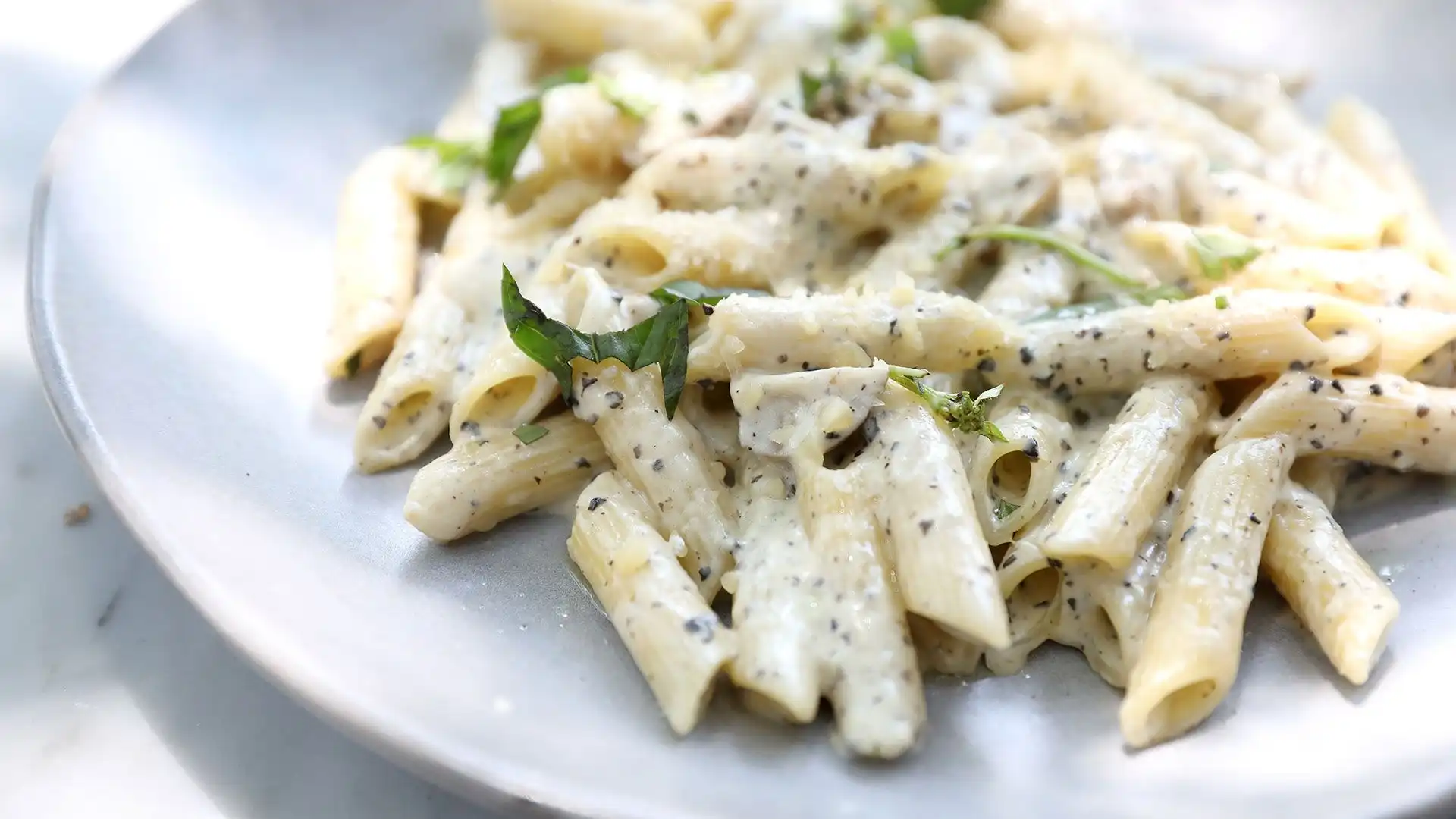 Prato de massa penne com alfredo e ervas, apresentando uma pasta deliciosa e cremosa, ideal para quem gosta de comida reconfortante e saborosa.