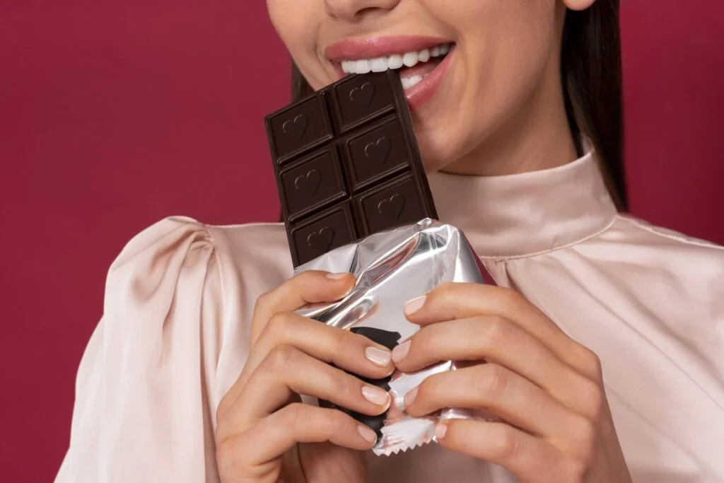 Mulher sorridente segurando barra de chocolate acabada de abrir, destaque para o chocolate de alta qualidade e gente feliz, ideal para quem busca dicas de chocolate.