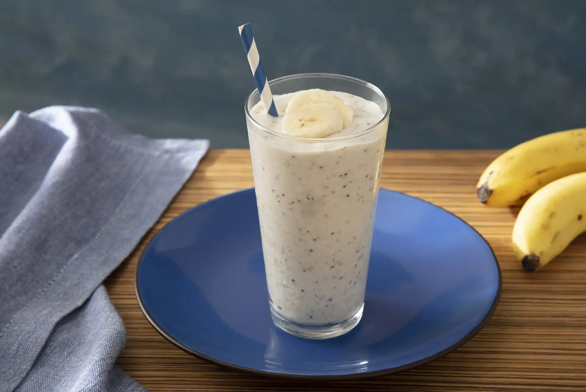 Vitamina de banana com leite e aveia em um copo alto, ao lado de bananas maduras, sobre uma mesa de madeira, perfeita para dieta saudável.