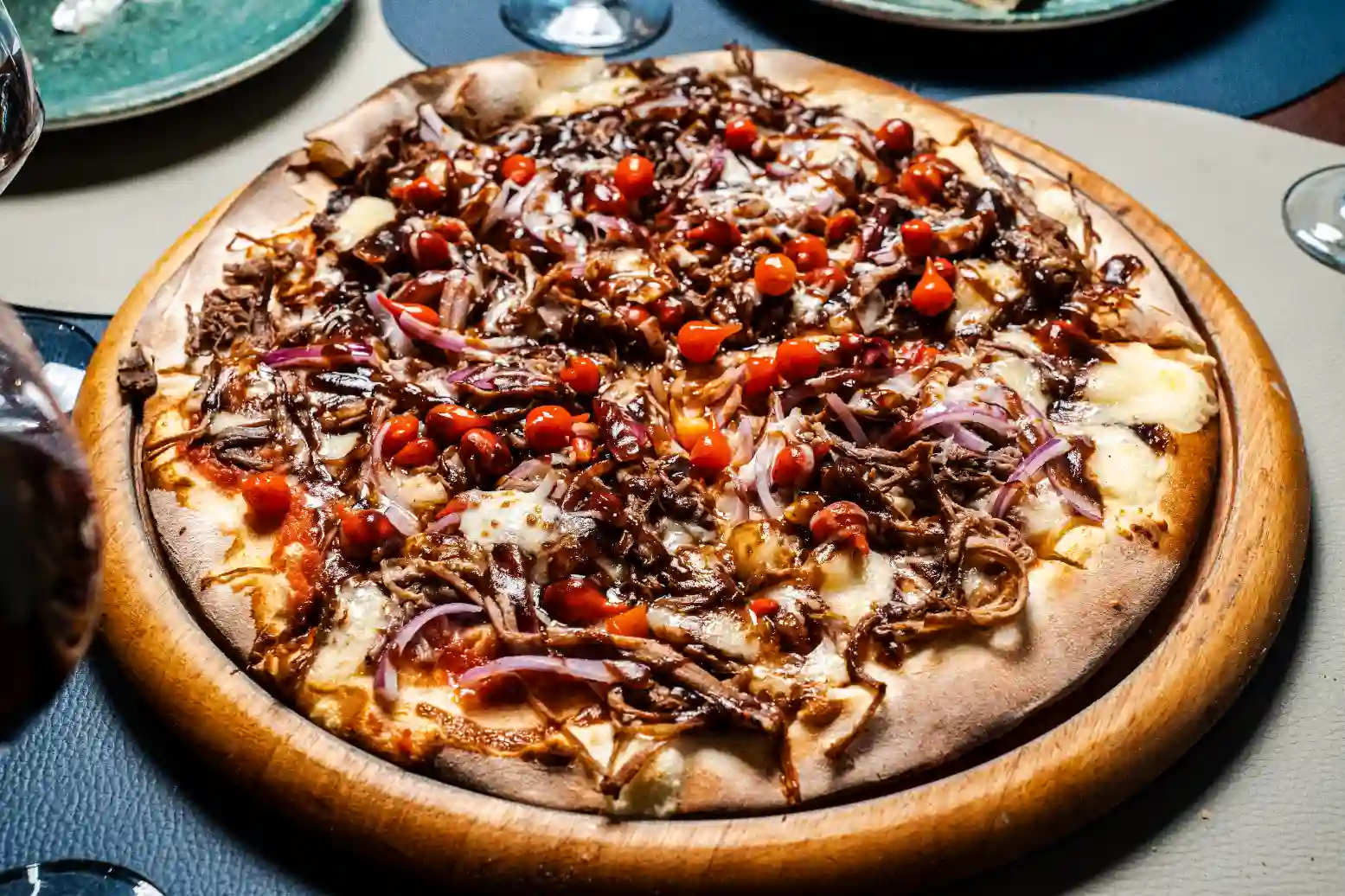 Pizza de carne desfiada com molho barbecue, queijo derretido, cebola roxa e pimentões, servida em uma tábua de madeira, ideal para pratos de steakhouse.