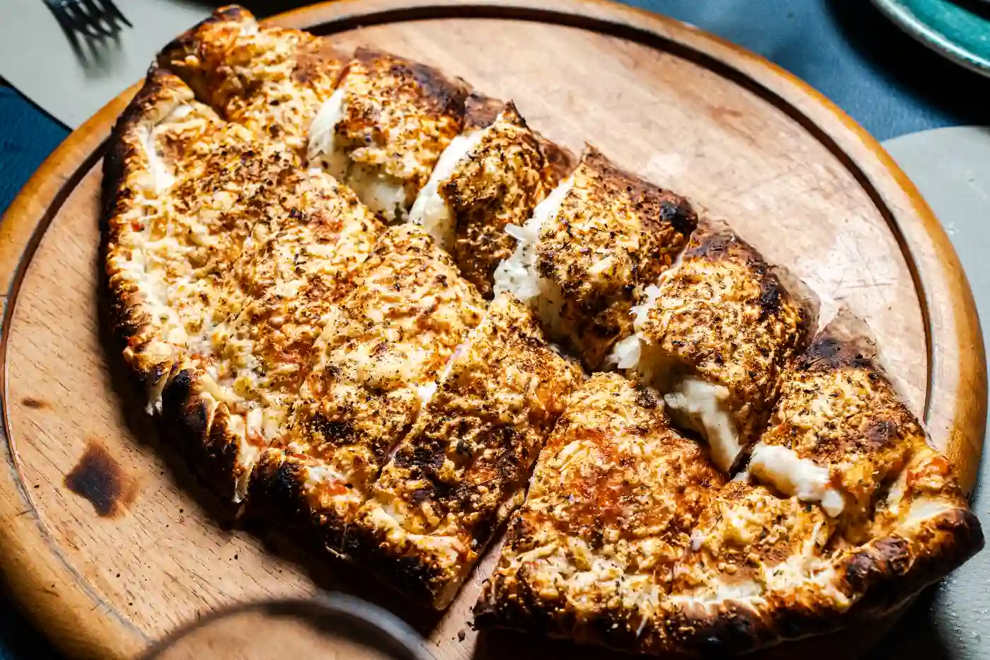 Imagem de uma deliciosa pizza assada com queijo, molho e temperos, cortada em fatias, servida sobre uma tábua de madeira em ambiente de restaurante.