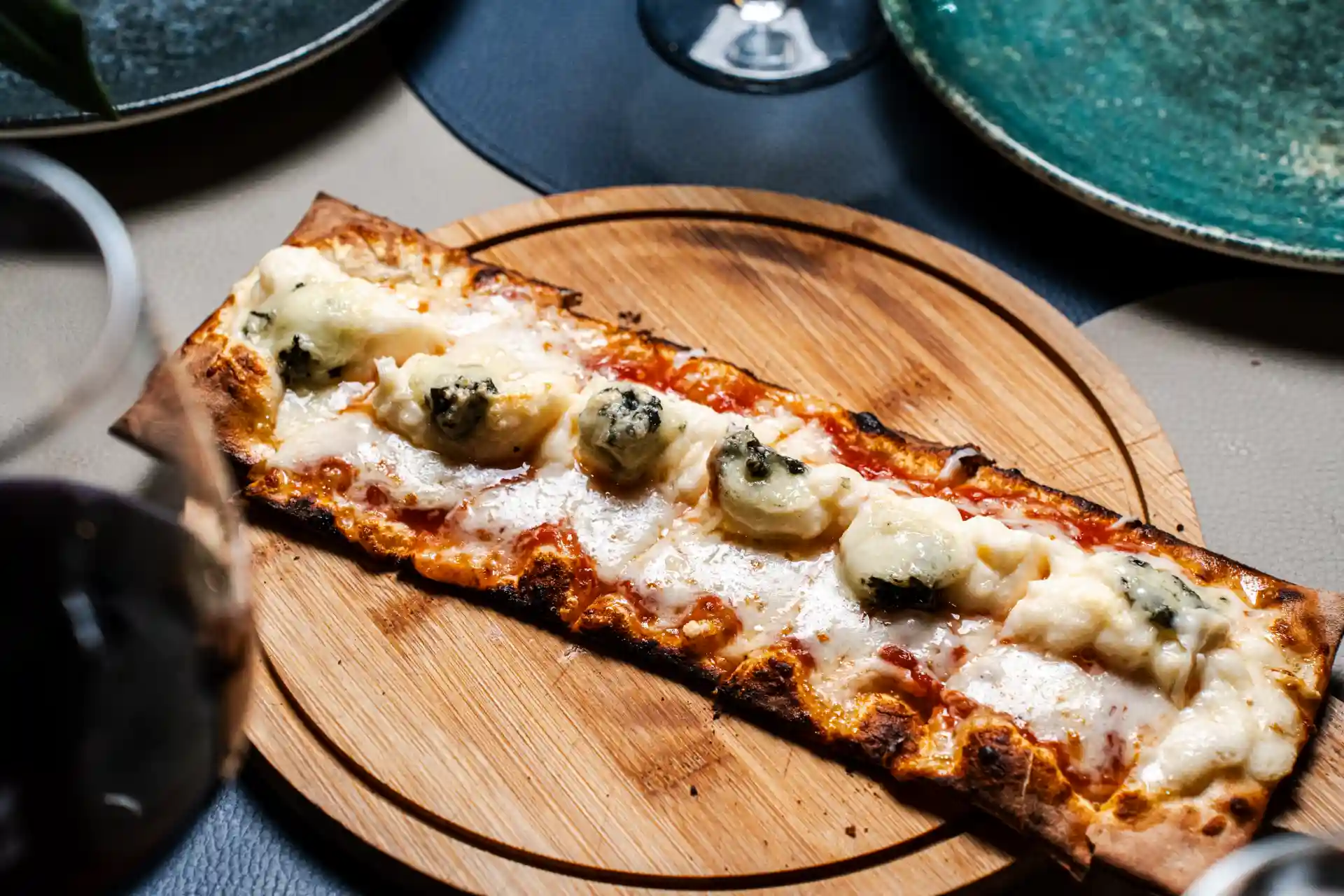 Pizza retangular de queijo e molho servida em uma tábua de madeira em um ambiente aconchegante.