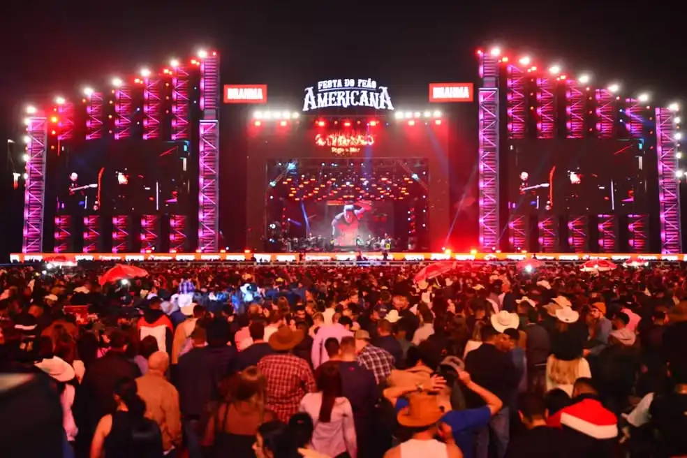 Grande público assistindo ao show no Festival de Folklore Americano, com palco iluminado e estrutura de iluminação em destaque, em uma noite de evento cultural e musical.